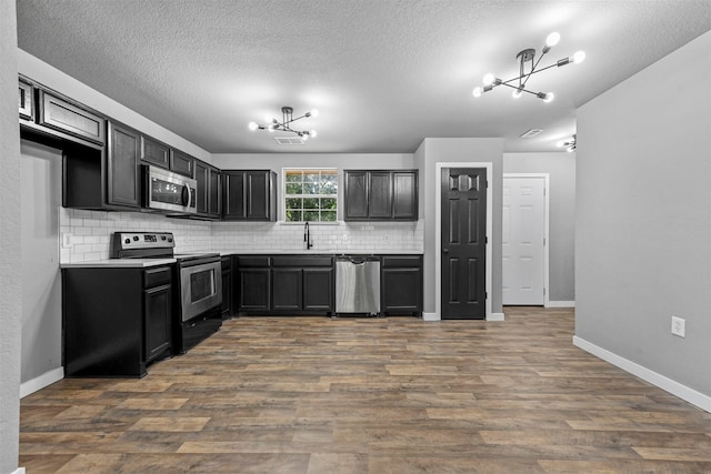 kitchen featuring a textured ceiling, backsplash, dark wood-type flooring, appliances with stainless steel finishes, and an inviting chandelier