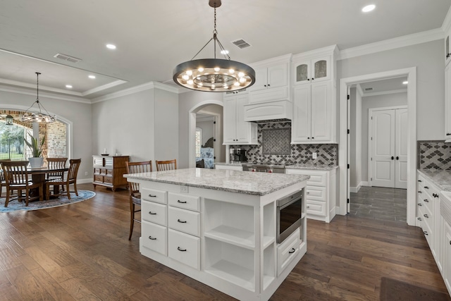 kitchen with white cabinetry, stainless steel microwave, a kitchen island, decorative light fixtures, and dark hardwood / wood-style floors