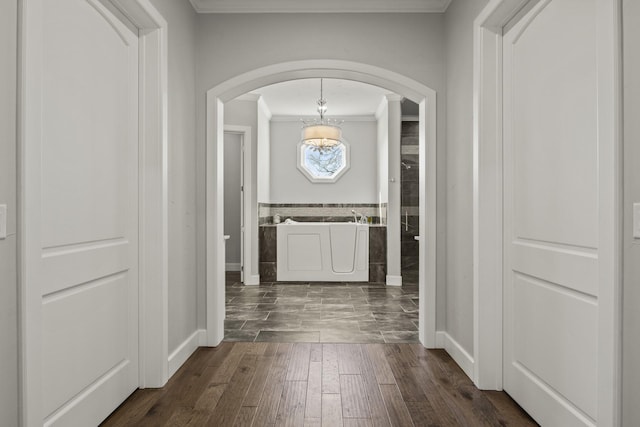 hall featuring crown molding, a chandelier, dark wood finished floors, arched walkways, and wainscoting