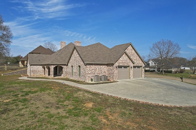 french country home with an attached garage, a chimney, cooling unit, and concrete driveway