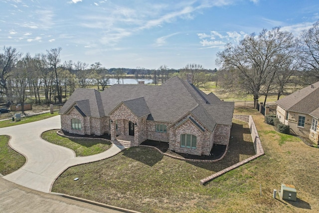 french country home with stone siding, a front yard, curved driveway, and roof with shingles