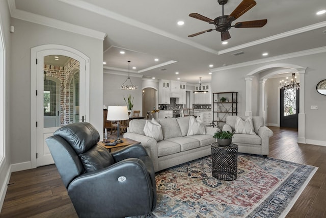 living area with a raised ceiling, ceiling fan with notable chandelier, arched walkways, dark wood-type flooring, and a healthy amount of sunlight