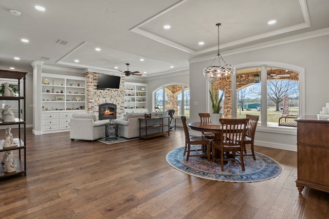 dining area featuring ceiling fan with notable chandelier, ornamental molding, a fireplace, and dark hardwood / wood-style flooring