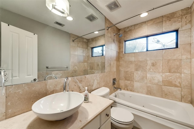 full bathroom featuring tile walls, vanity, tiled shower / bath, and toilet