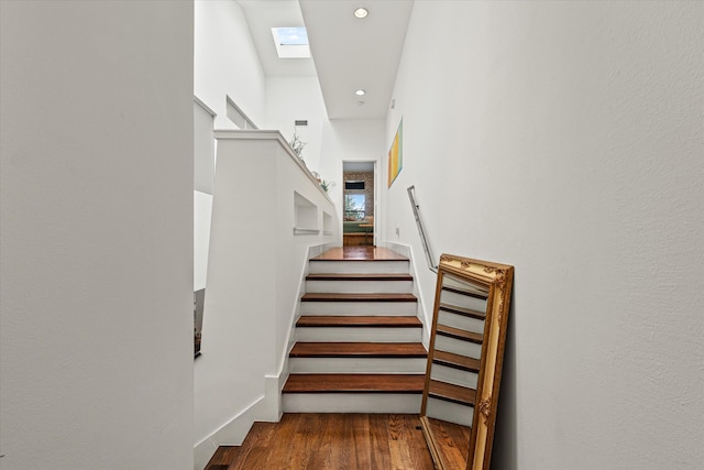 stairway featuring wood-type flooring, a high ceiling, and a skylight