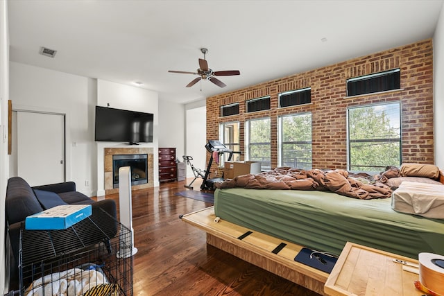 living room with ceiling fan, a tile fireplace, brick wall, and dark wood-type flooring