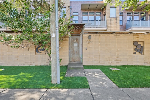 entrance to property featuring a balcony and a lawn