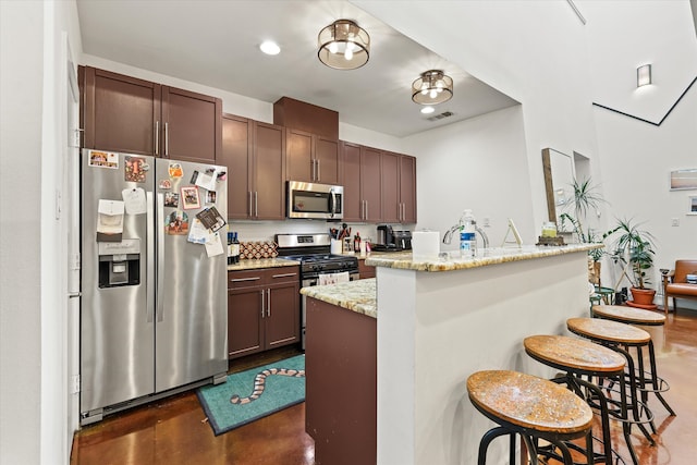 kitchen featuring a breakfast bar, light stone counters, a kitchen island with sink, appliances with stainless steel finishes, and dark brown cabinetry