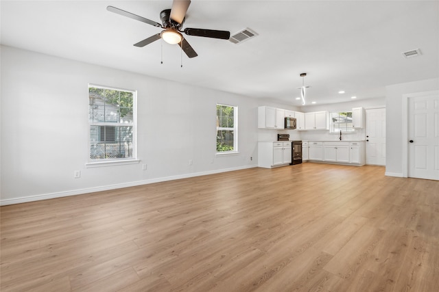 unfurnished living room featuring light wood-type flooring, sink, ceiling fan, and a wealth of natural light