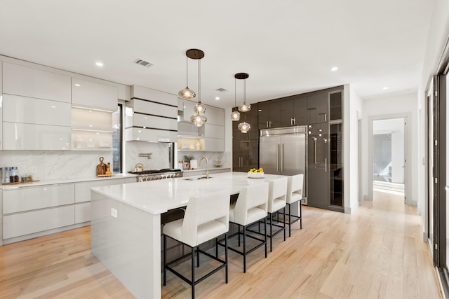 kitchen with decorative backsplash, light wood-type flooring, white cabinets, and a center island with sink