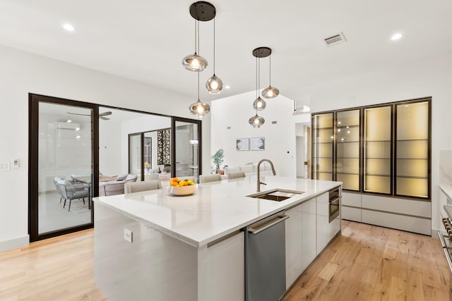 kitchen with hanging light fixtures, stainless steel dishwasher, sink, and an island with sink