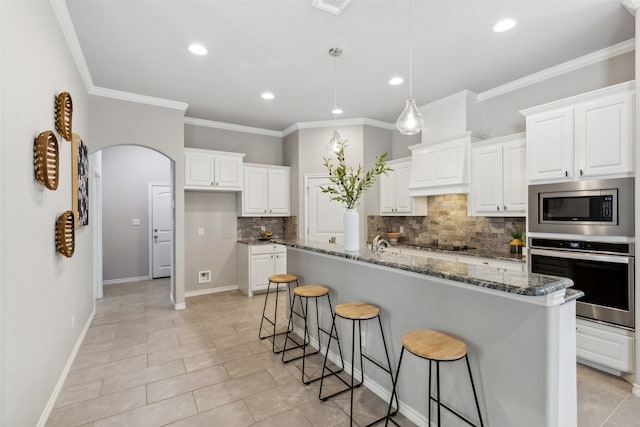 kitchen featuring white cabinetry, a kitchen island with sink, dark stone countertops, crown molding, and stainless steel appliances