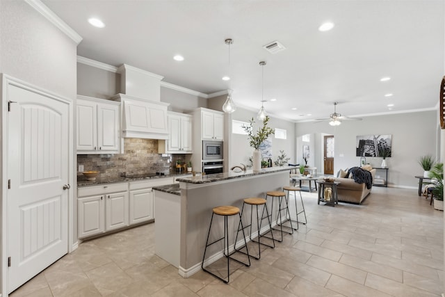 kitchen with a center island with sink, appliances with stainless steel finishes, a kitchen breakfast bar, white cabinetry, and dark stone countertops