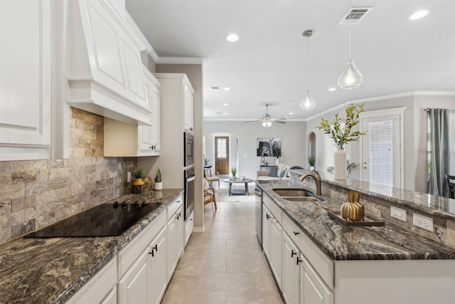 kitchen with sink, an island with sink, stainless steel appliances, pendant lighting, and white cabinets