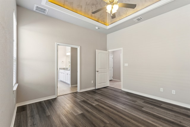 unfurnished bedroom with a raised ceiling, ceiling fan, ensuite bathroom, and dark hardwood / wood-style flooring