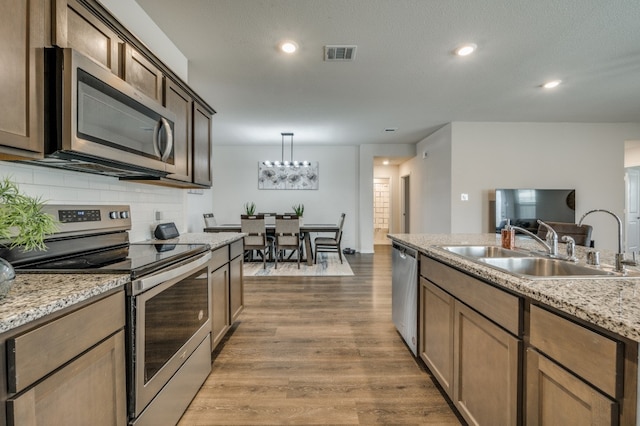 kitchen featuring sink, tasteful backsplash, wood-type flooring, decorative light fixtures, and appliances with stainless steel finishes