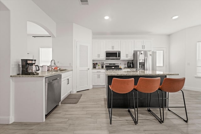 kitchen with light stone counters, sink, white cabinetry, appliances with stainless steel finishes, and a kitchen bar