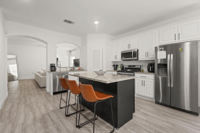 kitchen featuring light stone counters, white cabinets, light hardwood / wood-style flooring, appliances with stainless steel finishes, and a center island