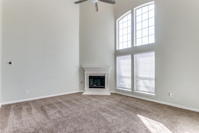 unfurnished living room with ceiling fan, carpet floors, and a towering ceiling