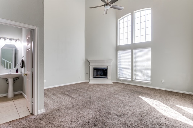 unfurnished living room with ceiling fan, light colored carpet, a towering ceiling, and sink