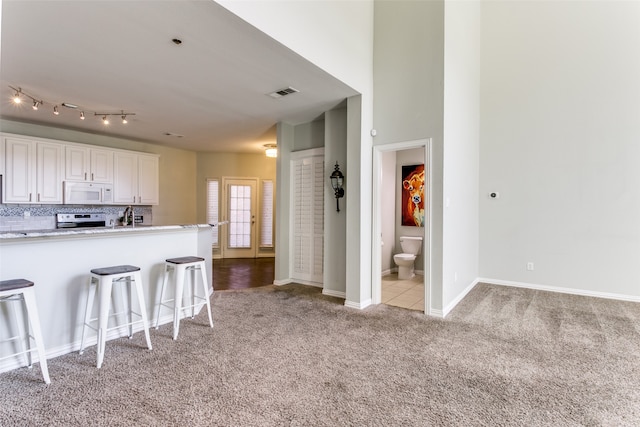 kitchen with white cabinets, tasteful backsplash, stainless steel range with electric stovetop, light carpet, and a breakfast bar area