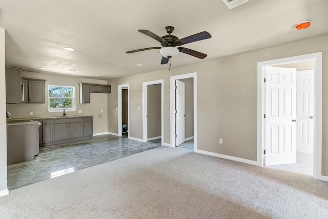 unfurnished living room featuring light carpet, ceiling fan, and sink