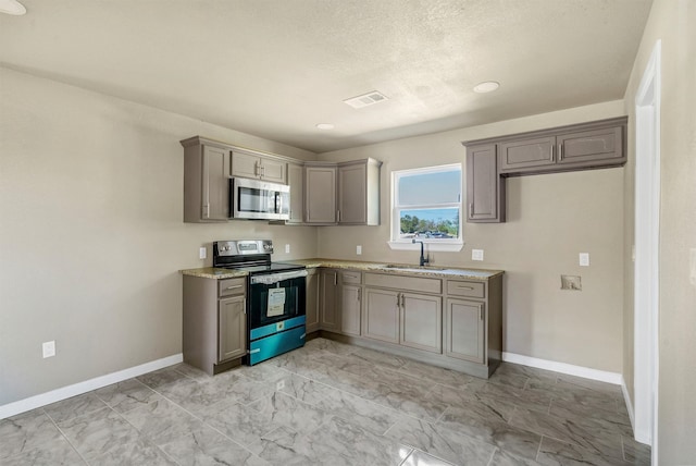 kitchen featuring appliances with stainless steel finishes, gray cabinetry, light stone counters, a textured ceiling, and sink