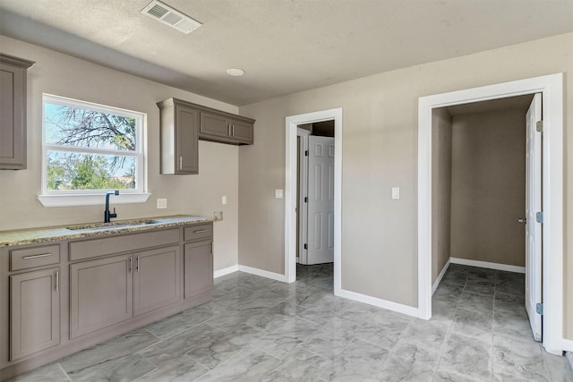 kitchen with light stone countertops, gray cabinetry, a textured ceiling, and sink