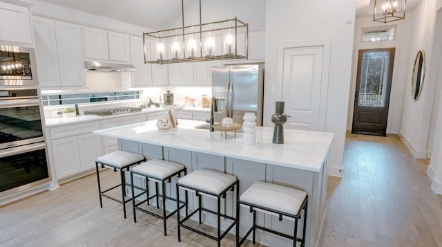 kitchen with stainless steel appliances, hanging light fixtures, a center island with sink, and white cabinets