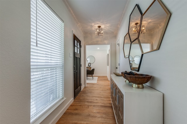 hall featuring crown molding, an inviting chandelier, and light wood-type flooring