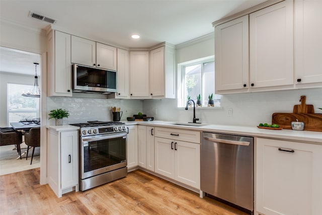 kitchen with ornamental molding, white cabinets, stainless steel appliances, and light hardwood / wood-style flooring