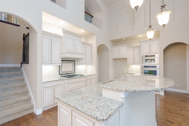 kitchen with pendant lighting, a towering ceiling, white cabinetry, and a center island with sink