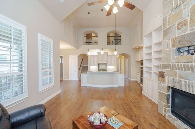 living room featuring high vaulted ceiling, a fireplace, ceiling fan, and light hardwood / wood-style flooring