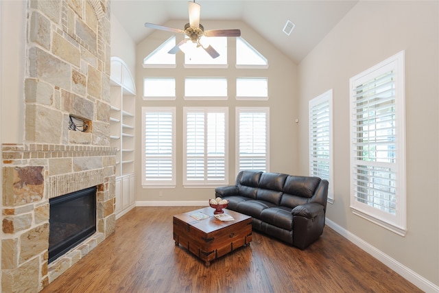 living room featuring ceiling fan, built in shelves, a stone fireplace, high vaulted ceiling, and hardwood / wood-style flooring