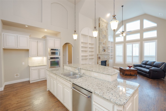 kitchen featuring sink, high vaulted ceiling, stainless steel appliances, a center island with sink, and a stone fireplace