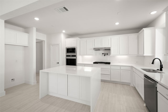 kitchen with appliances with stainless steel finishes, white cabinetry, sink, backsplash, and a center island