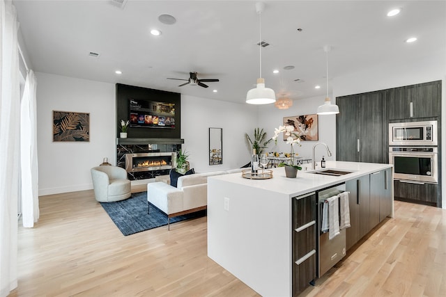 kitchen featuring sink, a center island with sink, stainless steel appliances, a fireplace, and light hardwood / wood-style floors