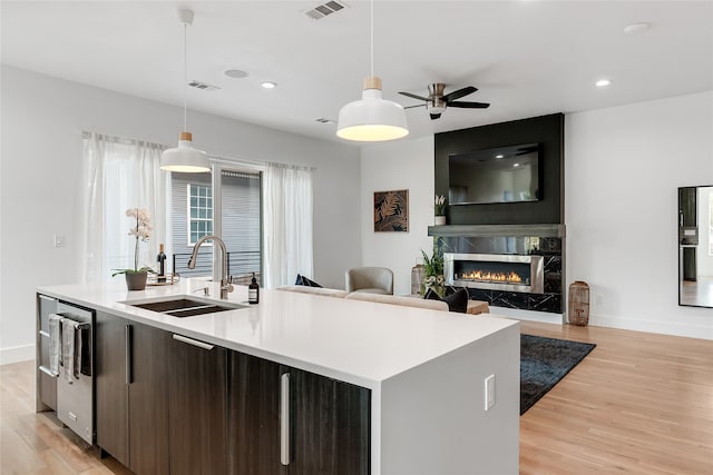 kitchen featuring light hardwood / wood-style floors, an island with sink, a fireplace, decorative light fixtures, and dark brown cabinetry