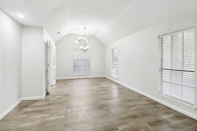 spare room featuring a notable chandelier, wood-type flooring, and lofted ceiling