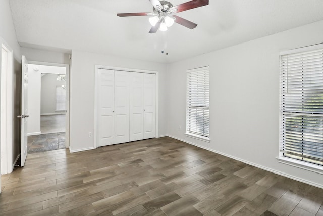 unfurnished bedroom with a closet, baseboards, wood finished floors, and multiple windows