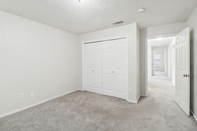 unfurnished bedroom featuring a textured ceiling, light colored carpet, and a closet