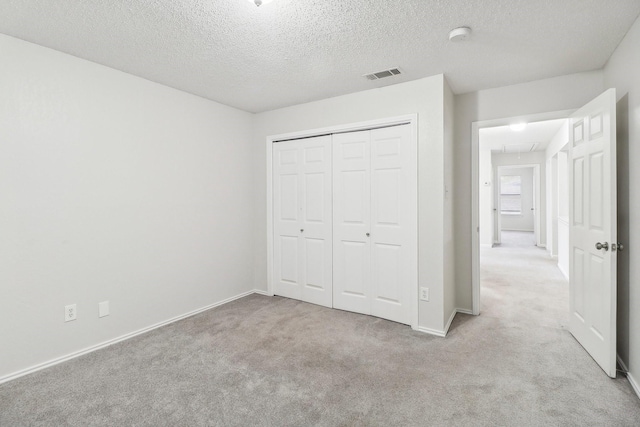 unfurnished bedroom with a closet, attic access, a textured ceiling, visible vents, and carpet