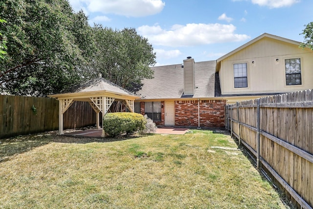 back of house with a chimney, a fenced backyard, a gazebo, brick siding, and a lawn