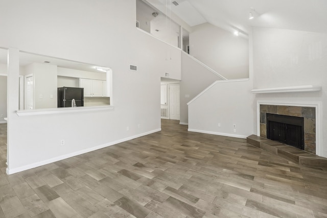 unfurnished living room featuring hardwood / wood-style flooring, a tiled fireplace, and high vaulted ceiling