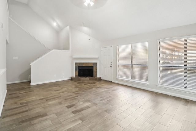 unfurnished living room featuring vaulted ceiling, ceiling fan, a tile fireplace, and light hardwood / wood-style floors