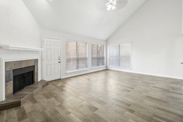 unfurnished living room featuring a tiled fireplace, a ceiling fan, vaulted ceiling, and wood finished floors