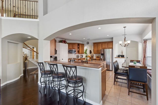 kitchen with hanging light fixtures, kitchen peninsula, stainless steel appliances, light wood-type flooring, and a notable chandelier