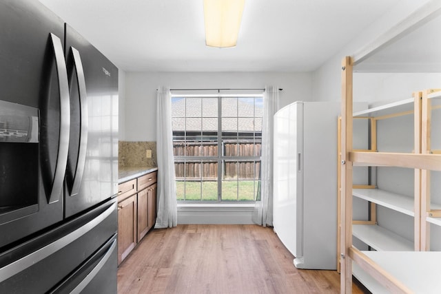 kitchen featuring light stone counters, stainless steel fridge with ice dispenser, tasteful backsplash, white fridge, and light hardwood / wood-style flooring