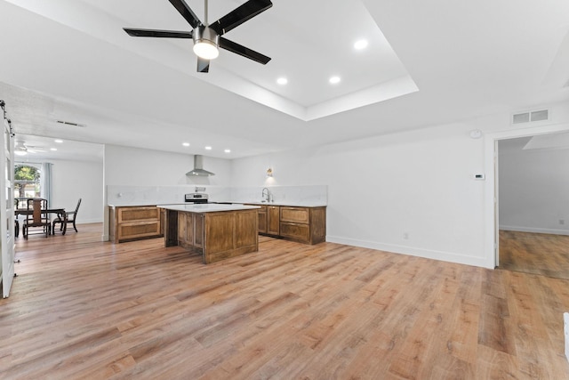 kitchen featuring light hardwood / wood-style floors, a center island, ceiling fan, and wall chimney range hood