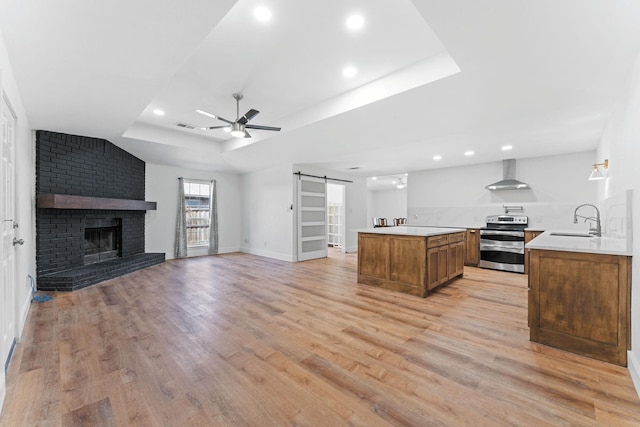 kitchen with electric stove, a barn door, wall chimney exhaust hood, light hardwood / wood-style flooring, and sink